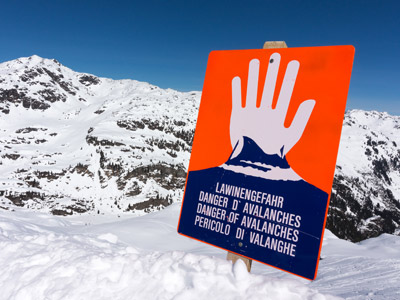 Ein Warnschild über Lawinengefahr vor schneebedeckten Bergen.
